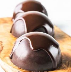 three gorgeous chocolate bombs with hot fudge sauce dripping over them, atop a gold platter