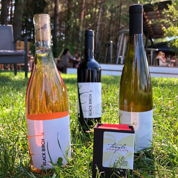 a small box of Tangle Chocolate thins and three bottles of Black Birch Wine of Massachusetts, sitting in the grass