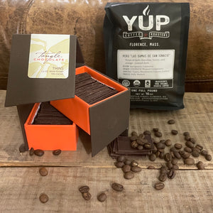 a large open box of chocolate thins by Tangle Chocolate and a bag of YUP coffee, with some chocolate thins and coffee beans strewn around, against a neutral brown and gray background