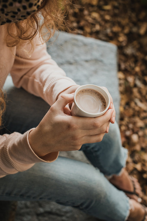 Woman in jeans holding white mug of hot chocolate outside