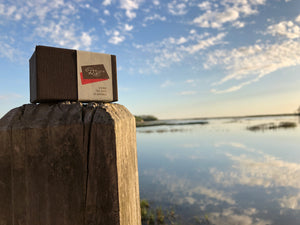 a brown box with brown and red details sitting on a wooden stump, against a reflective body of water in the background