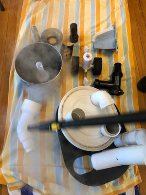 Rabbi Shlomo Yaffe kashering some food manufacturing equipment, including an industrial steam cleaner laying across a vertically-striped blue, orange, and yellow sheet.