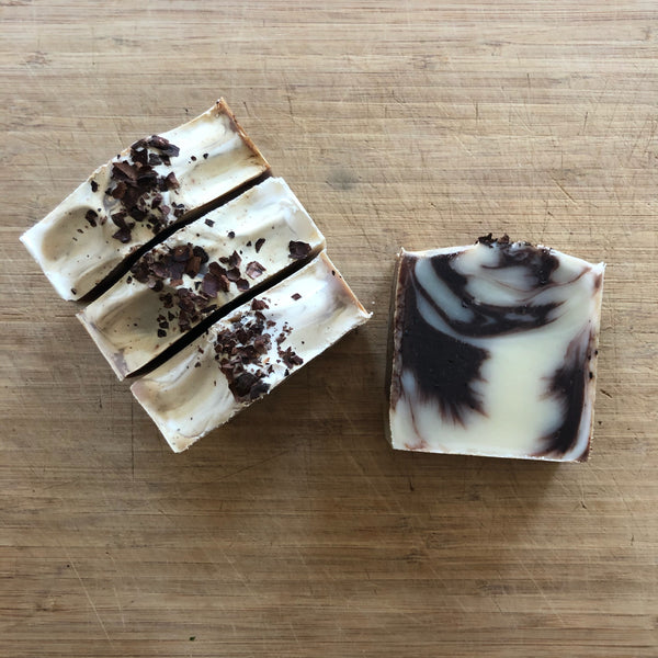 Tangle Chocolate Soap bars made by Amherst Soaps, with swirls of deep brown and cream topped with cocoa husks against a wooden table