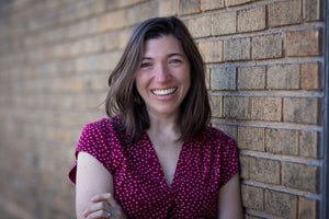 smiling white woman with brown hair leaning on brick wall