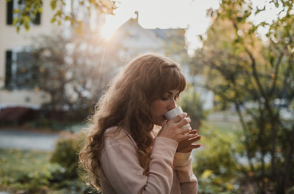 young woman with long auburn hair drinking mug of hot chocolate outside, surrounded by 