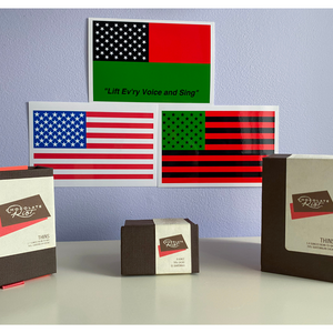 three different-sized boxes of Tangle Chocolate thins atop a white table, with three different versions of American flag stickers on the white background wall