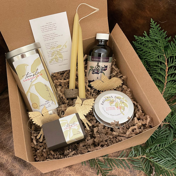 a large open gift box containing a large silver tin, small white tin, syrup bottle, small brown Tangle Chocolate box, candlesticks, and a poem on white paper